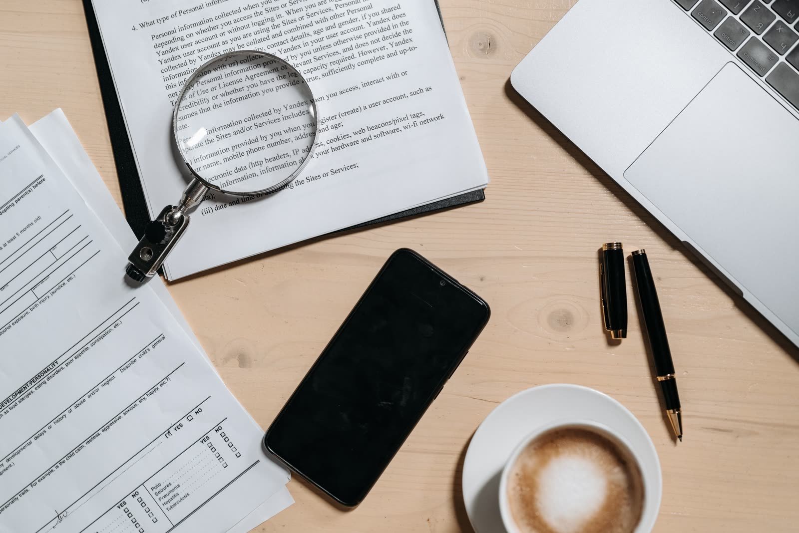 Workspace with documents, laptop, phone, coffee, and magnifying glass